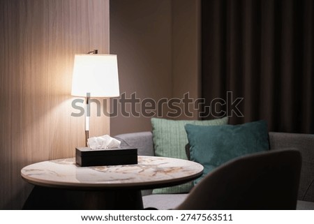 Cozy interior corner with a warm table lamp, marble round table, tissue box, and soft cushions creating a relaxing ambiance.