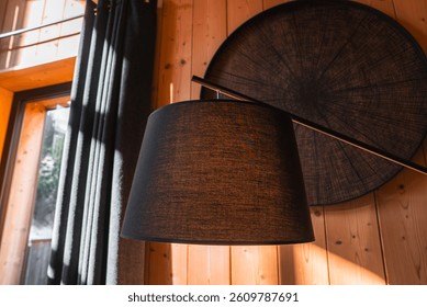 Cozy interior featuring a black lampshade, wooden panel walls, a circular wall decoration, and natural light from a window with alpine views.