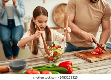 In a cozy kitchen, parents and kids connect while preparing a fresh vegetable salad, cherishing family time and cooking together in a warm atmosphere - Powered by Shutterstock