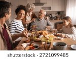 A cozy kitchen table scene shows a multi-generational family enjoying a meal together. Laughter, conversation, and shared dishes create a warm, inviting moment of home life and togetherness.