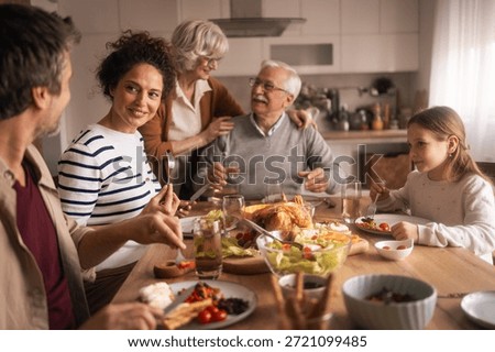 A cozy kitchen table scene shows a multi-generational family enjoying a meal together. Laughter, conversation, and shared dishes create a warm, inviting moment of home life and togetherness.