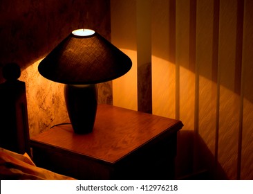 Cozy Lamp On A Night Stand Near A Bed (shining In The Darkness)