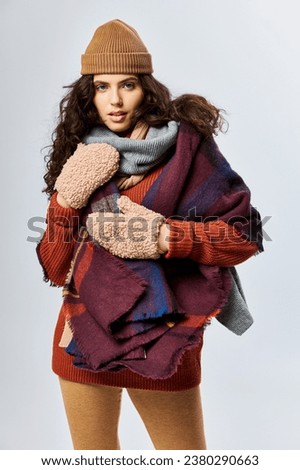 cozy layers, curly young woman in layered clothes with warm scarf and mittens on grey backdrop