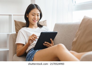 Cozy lifestyle concept, Young woman lying on couch and using tablet to surf social media at home. - Shutterstock ID 2170524983
