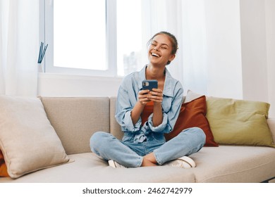 Cozy Living: A Happy Woman Holding a Mobile Phone on a Sofa at Home - Powered by Shutterstock