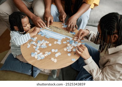 Cozy living room with family engaging in puzzle activity, children and adults bonding and sharing time. African American family sitting around wooden round table piecing together puzzle - Powered by Shutterstock