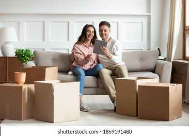 In Cozy Living Room Heap Of Carton Boxes, Couple Sit On Sofa With Tablet Buying Furniture On Internet, Search Design Ideas, Enjoy Rest At New Home. E-commerce House Services, First Flat Owners Concept