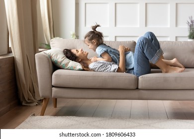 In cozy living room on comfy couch lying mother and her little cheery daughter. Kid girl lay on mom enjoy playtime and positive communication. Funny time together at home, love and protection concept - Powered by Shutterstock