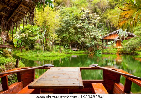 A cozy lodge nestled in the lush Amazon rainforest of Mindo, Ecuador. A serene lake surrounded by exotic plants and vibrant lianas.