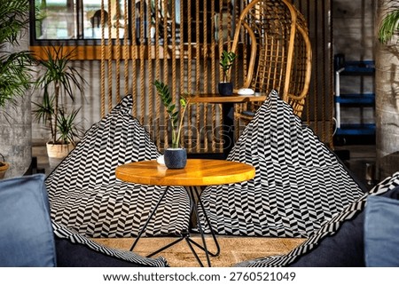 Cozy lounge space featuring patterned bean bag chairs, a wooden coffee table, and natural decor elements. The modern boho-style interior includes plants, textured walls, and warm lighting, creating a relaxing and inviting atmosphere perfect for socializing or unwinding.