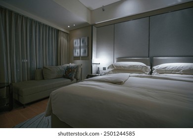 A cozy and luxurious bedroom featuring a large bed with plush white bedding and a padded headboard. The room is dimly lit, creating a relaxing ambiance.  - Powered by Shutterstock