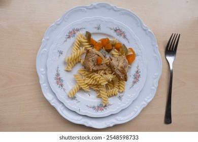 cozy meal of pasta, stewed meat, and vegetables on classic ceramic plate with floral design, served with fork - Powered by Shutterstock