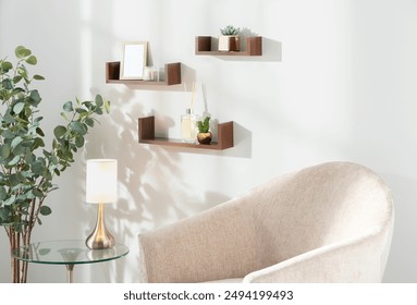 Cozy minimalist living space with floating wooden shelves, a stylish glass side table, framed photos, lush green plants, and a beige armchair, creating a serene and inviting atmosphere for relaxation. - Powered by Shutterstock