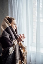 Cozy Mood, Baby Its Cold Outside. Young Woman Standing Near Window With Plaid, Drinking Coffee Or Tea, Looking Outside, Relaxing In Her Living Room