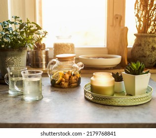 Cozy Morning With Lemon And Ginger Tea At Kitchen Table With Mugs, Candle And Herbs At Window Background. Warming Hot Drinks.  Front View.