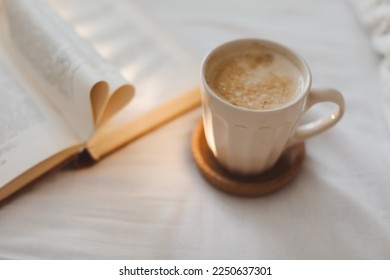 Cozy morning still life with a coffee cup, needles and a book with pages folded into a heart shape in bed - Shutterstock ID 2250637301