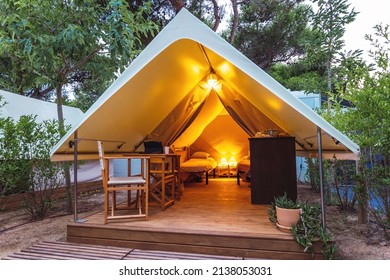 Cozy open glamping tent with light inside during dusk. Luxury camping tent for outdoor summer holiday and vacation. Lifestyle concept - Shutterstock ID 2138053031