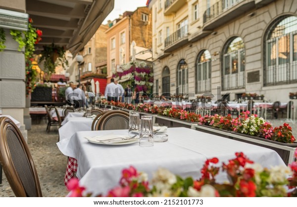 Cozy outdoor restaurant in Belgrade city center in\
summer, Serbia. Empty tables set for a meal with empty empty\
glasses and plates