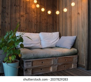 Cozy Pallet Couch On Balcony With Lamps Above During Night.