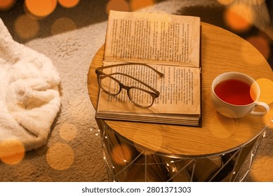 Cozy reading setup with open book, eyeglasses, and cup of tea on wooden table
