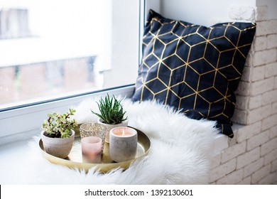 Cozy real home decoration, burning candles on golden tray with pillow on white faux fur on windowsill