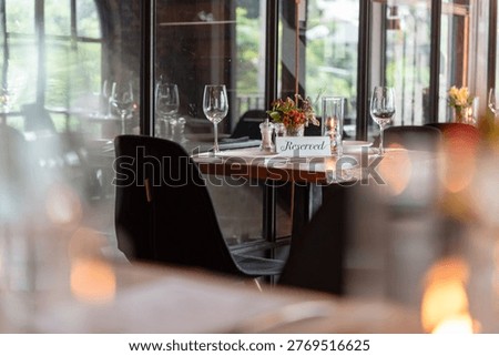 Cozy restaurant setting with a reserved table, elegantly set with wine glasses and a small floral centerpiece by a window.