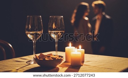 A cozy romantic dinner setup with two wine glasses, candles, and a couple in the background.