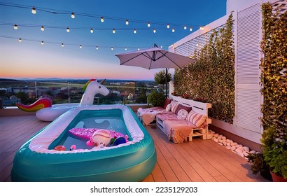 cozy rooftop patio with wooden pallet furniture, vertical garden and inflatable pool at warm summer evening - Shutterstock ID 2235129203
