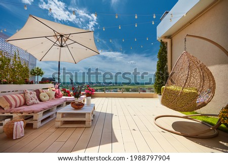 a cozy rooftop patio with wooden pallet furniture and hanging swing chair at sunny summer day