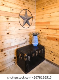A cozy rustic corner featuring a black vintage trunk, decorative ceramic vase with greenery, and warm pine wood walls. Industrial farmhouse decor in a cabin-style interior.