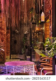 A cozy, rustic dining corner featuring hanging roots, lush plants, warm lanterns, and patterned tile flooring.