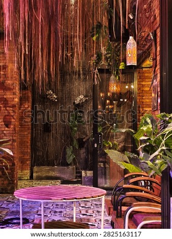 A cozy, rustic dining corner featuring hanging roots, lush plants, warm lanterns, and patterned tile flooring.
