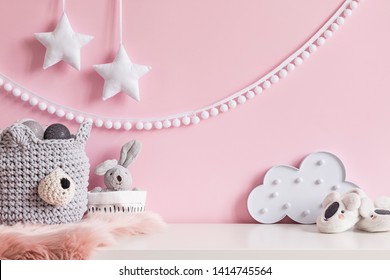 Cozy scandinavian newborn baby room with gray basket ,white stars lamp, cloud, plush rabbit and children accessories. Stylish interior with pink walls and haniging white garland.Template. Copy space. 