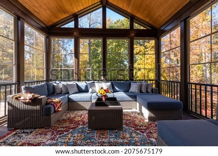 Cozy screened porch with contemporary furniture and flower bouquet in a vase, autumn leaves and woods in the background.
