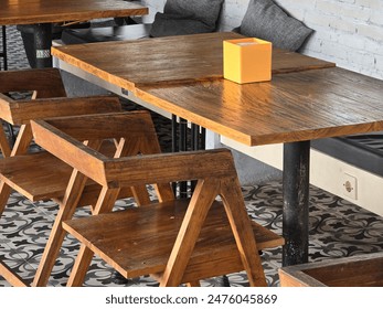 A cozy seating area in a modern café featuring wooden tables and chairs, gray cushions, and a lush green plant wall. Ideal for themes related to interior design and comfortable dining spaces. - Powered by Shutterstock