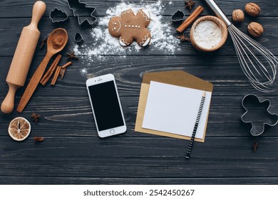 A cozy setup for Christmas baking with gingerbread cookies, cinnamon, and a whisk on a rustic wooden table. Includes a smartphone, rolling pin, and blank note for a festive touch. - Powered by Shutterstock