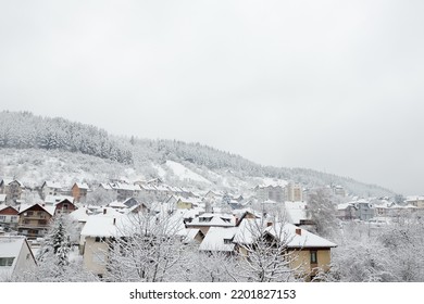 Cozy Small European Town On A Hillside On A Snowy Winter Day. The Village Houses And Forest Are Covered With Fresh Snow.