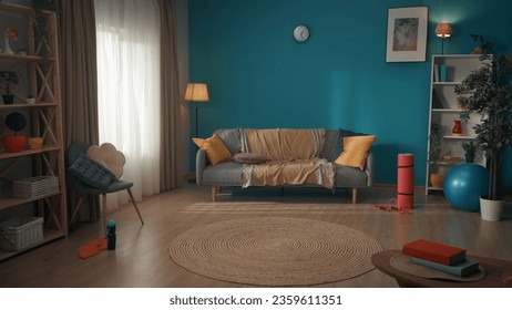 A cozy small room with a modern design. Filled with daylight accented by a blue wall. The room is filled with various decor. On the floor lies sports equipment for fitness. Living room. - Powered by Shutterstock