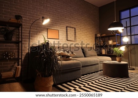 Cozy sofa, coffee table and glowing lamps in interior of living room at night