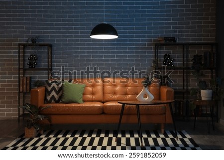 Cozy sofa, coffee table and glowing lamps in interior of stylish living room in evening