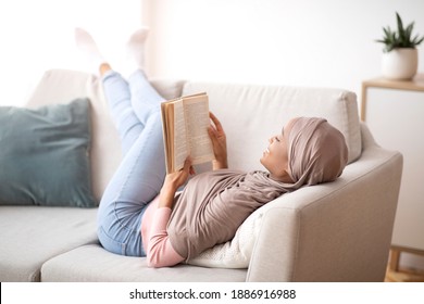 Cozy stay at home activities. Black young woman in hijab reading her favorite book, lying on sofa in living room. African American lady in Muslim headscarf enjoying interesting story on Sunday morning - Powered by Shutterstock