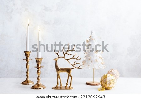Cozy still life with burning candles, figure of deer and Christmas decorations on pastel light background. Christmas composition for home interior
.