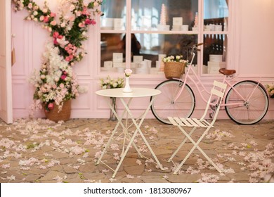 Cozy street with flowers and French-style cafe table. Empty cafe terrace with white table and chair. Pink exterior of the cafe restaurant. interior Street cafe. Decor facade of coffeehouse with bike.  - Powered by Shutterstock