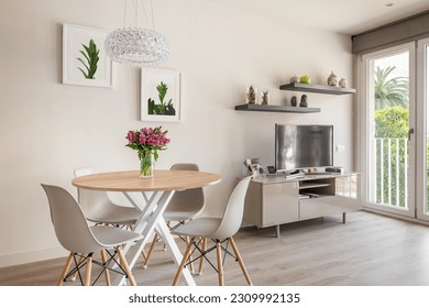 Cozy stylish living room with a round dining table, TV and panoramic windows and decorative accessories. The concept of a modern urban apartment for newlyweds