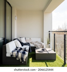 Gemütlicher und sonniger Balkon mit synthetischem Gras und stylischem RattanEcksofa mit dekorativen Kissen und Rattantisch