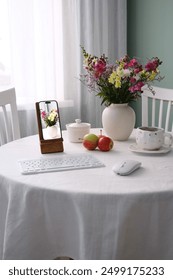 A Cozy Table Setting Featuring Fresh Flowers Along with Essential Tech Gadgets and Items