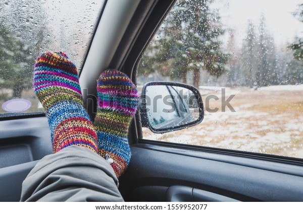 cozy travel time in road trip, feet in\
colorful socks in the car in rainy autumn\
day