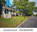 A cozy two-story house painted in deep green, surrounded by lush greenery. White shutters and a porch contrast with the dark walls, creating a welcoming atmosphere in a tranquil suburban neighborhood.