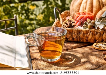 Cozy warm autumn composition with cup of hot tea, burning candle, open book and pumpkins on wooden background. Autumn home decor. Fall mood. Thanksgiving. Halloween.