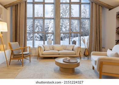 cozy warm home interior of a chic country chalet with a huge panoramic window overlooking the winter forest. open plan, wood decoration, warm colors and a family hearth
